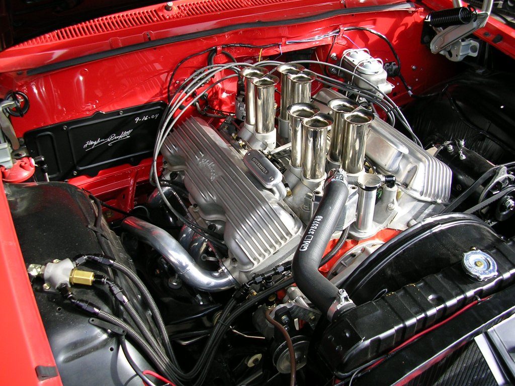 A close-up of a red car engine featuring a large engine block and an oversized exhaust pipe.