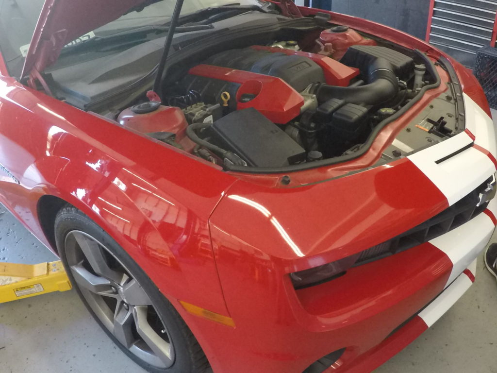 A red car with its hood open, revealing the engine lying on the ground beside it.